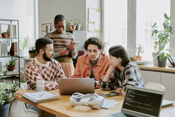 Biracial young IT specialists discussing steps of solving problem with coding in office
