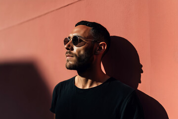 Fototapeta premium Stylish Young Man in Sunglasses Leaning Against Pink Wall – Urban Fashion and Modern Street Aesthetic