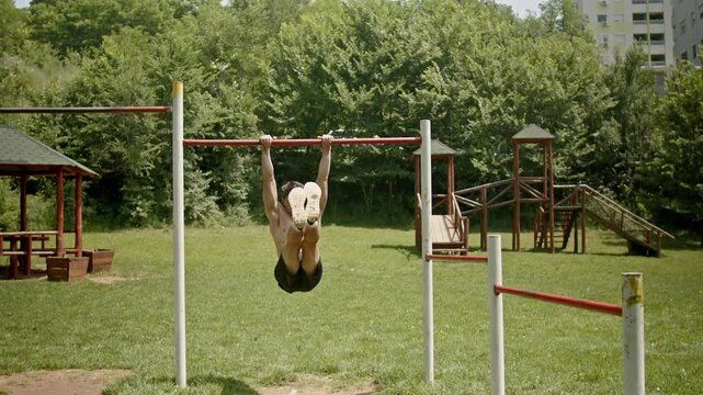 Young muscular sportsman doing an L-sit on a horizontal bar outdoors in a neighborhood park during the summertime. The exercise takes core strength, concentration, and balance.