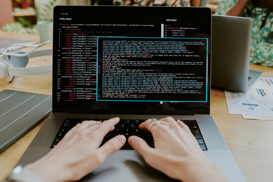 Point of view shot of unrecognizable female hands editing code lines on laptop at desk in office