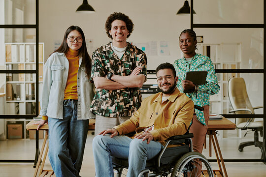 Medium full shot of biracial team dressed in casual clothes smiling at camera while working in cozy office - Powered by Adobe