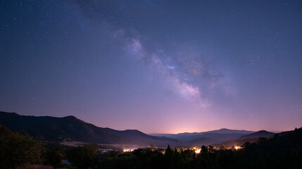 Night sky over mountains with the milky way galaxy and city lights in the distance view from afar