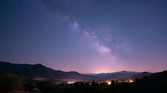 Night sky over mountains with the milky way galaxy and city lights in the distance view from afar