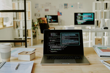 Medium close up of laptop with codes on screen on top of wooden table in office