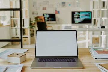 Medium close up of silver laptop with white screen surrounded by copybooks in modern office of IT company