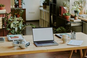 High angle shot of wooden table with laptop and VR headset located in comfortable office zone with green plants