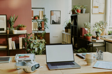 Fototapeta premium Laptop with white screen and documents on top of wooden table located in work zone of IT office