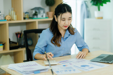 An Asian woman employee focused on completing the monthly sales summary with dedication.