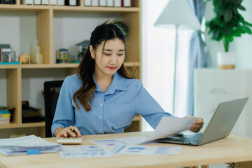 An Asian woman employee focused on completing the monthly sales summary with dedication.