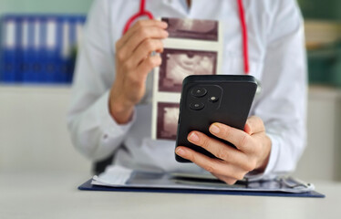 Doctor consulting patient while reviewing ultrasound images and using smartphone in modern medical office