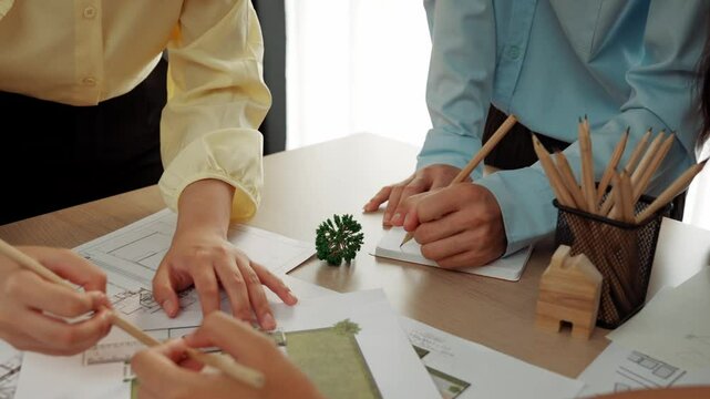 Smart architect and safety engineer discussion about building blueprint on table with architectural document, measurement tools and wooden block scatter around at modern office. Closeup. Delineation.