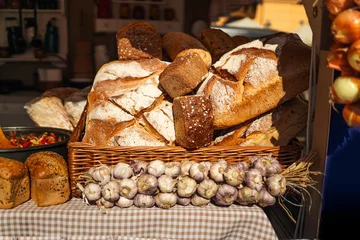 Fototapeten A variety of freshly baked loaves of bread are neatly arranged on a display table at a market. The loaves are golden-brown with crisp crusts and sit in a basket with a checkered cloth. Lights hang © Shi 