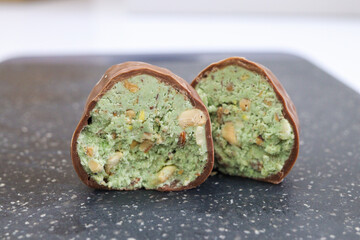 Cut chocolate dubai candy with green filling, placed on black granite surface. Close-up view of gourmet candy with visible texture and nut pieces. Minimalist kitchen background. High quality photo