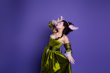 Elegant young woman posing in green historical dress with violet background