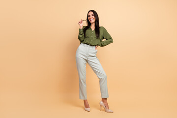 Fototapeta premium Confident young businesswoman posing in green shirt and light trousers on beige background, showcasing professional and stylish attire