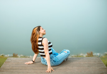 a young woman, wearing a black-and-white striped sleeveless top, ripped blue jeans, and black...