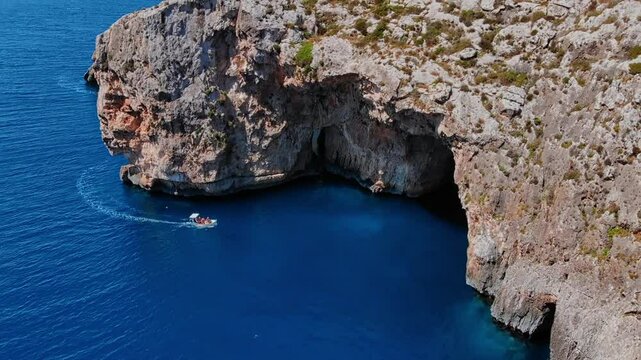 Aerial top view Blue Grotto in Malta. Pleasure boat with tourists runs. Natural arch window in rock