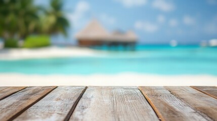 Fototapeta premium A rustic wooden table sits prominently in the foreground, providing a perfect view of a serene tropical beach. Clear blue waters lap gently at the shore under a bright sky