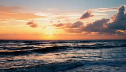 Obraz premium a vibrant sunset casts golden and orange hues across the rippling ocean surface beneath dramatic cloud formations.