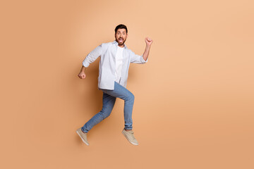 Young man jumping joyfully in a casual striped shirt and blue jeans against a beige background,...