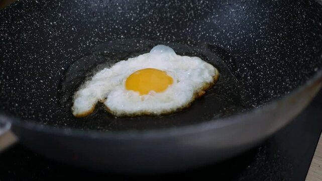 Cooking fried eggs sunny side up with a sizzling oil in frying pan.