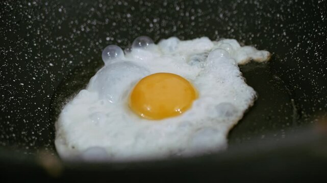 Cooking fried eggs sunny side up with a sizzling oil in frying pan.