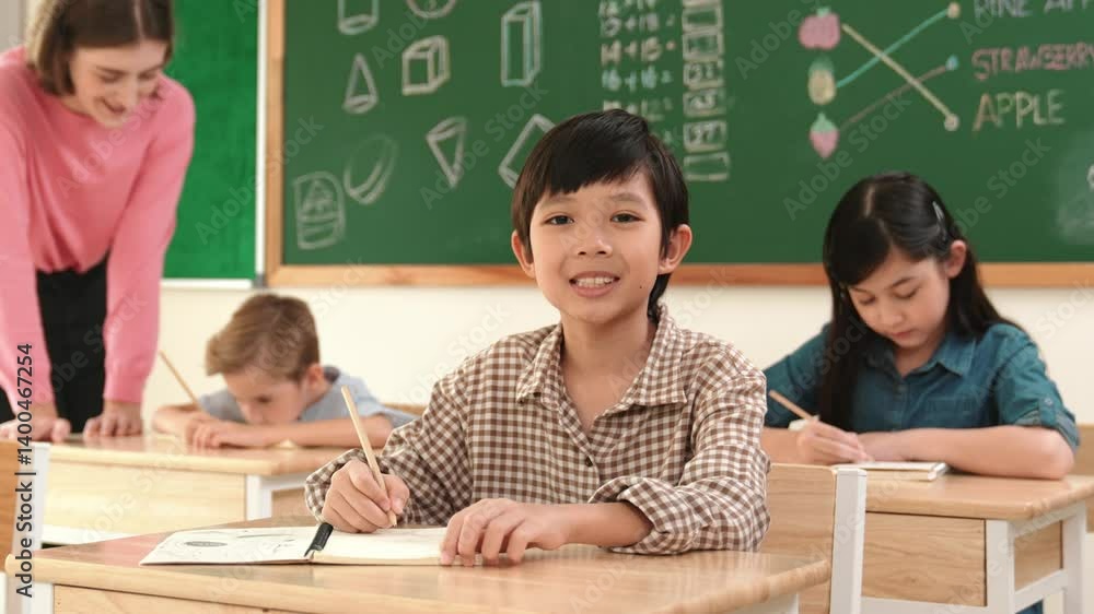 Aufkleber asian smart boy smiling to camera while student writing answer in answer sheet. multicultural studen