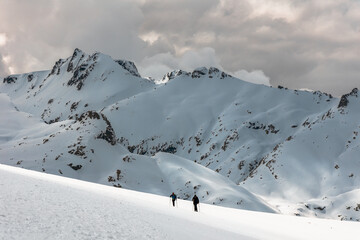 Two hikers climbing a snowy slope toward jagged alpine peaks in Sierra de Gredos, Spain, under...