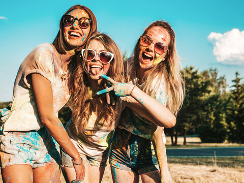 Three happy beautiful female making party at Holi festival in summer time. Young smiling women friends having fun after music event at sunset. Positive models going crazy in sunglasses at sunset