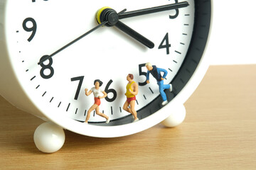Miniature people toy figure photography. Running daily routine concept. A team group runner jogging above clock, isolated on white background.