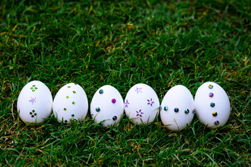 white Easter eggs adorned with colorful sequins and arranged On Green Grass