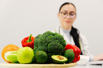 A nutritionist takes notes and works at a computer in a bright medical office. Fresh vegetables and...