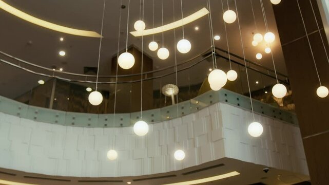 Low angle view of multiple glowing spherical lights hanging from ceiling in upscale hotel lobby with stylish interior