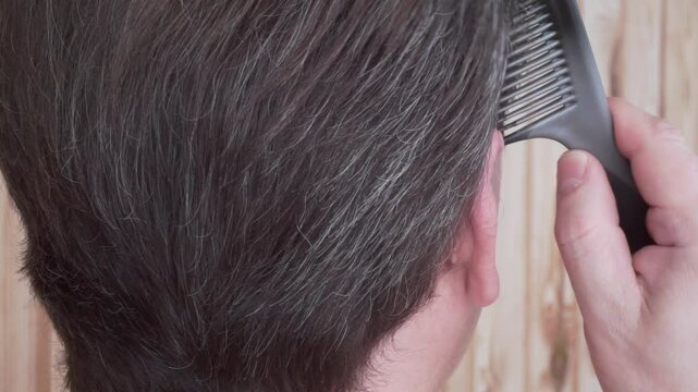 Grey hair in a man. Close-up of an adult male head with hair starting to turn grey. First signs of grey hair in a man. A man brushing and styling grey hair. Rear view of mans head. Beauty concept