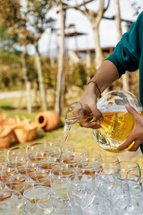 A person is pouring white wine from decanter to glasses before outdoor party