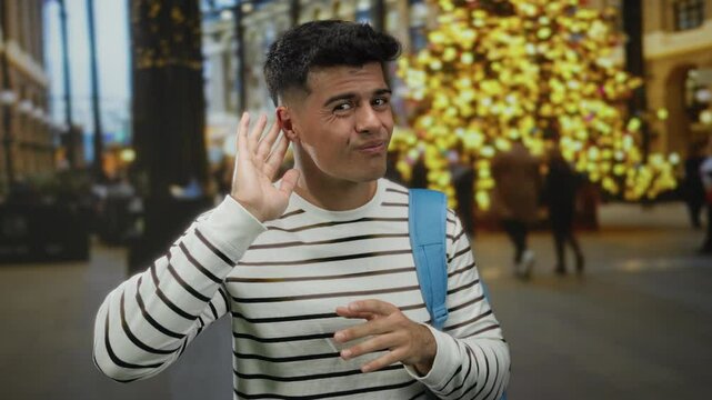Young man gestures quizzically against a backdrop of city lights in an urban street scene, highlighting an intriguing expression and casual fashion in a nighttime environment.