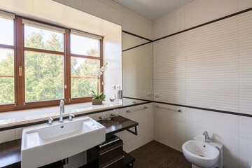 bright, well-lit bathroom with a large window, a modern tub, sink, and bidet, all elegantly designed.