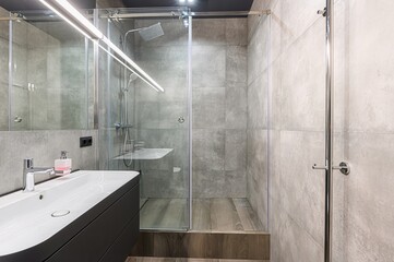 Modern bathroom featuring gray tiles, a sleek vanity with a white sink, and a glass-enclosed...