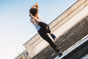A woman mid-workout on stone steps performs a standing oblique crunch, balancing strength and focus...