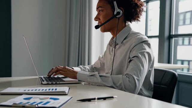 Corporate operator in headset working in customer support service on helpline telesale talking using laptop in business office. Agent of call center advises the client by answering questions. Close up