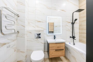 Modern bathroom with white and gold marble tiles, floating vanity, lighted mirror, and black fixtures. Clean, stylish design.