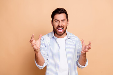 Young man expressing frustration with expressive gestures on a beige background in a casual striped shirt