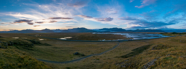 Icelandic landscape: mountains, river, grassland, and dramatic sky.