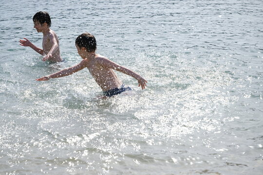 two cheerful teenagers, boys swimming in sea, ocean waves, Summer fun beach, family Water activities, Kids splash and swim, aquatic adventures, safety