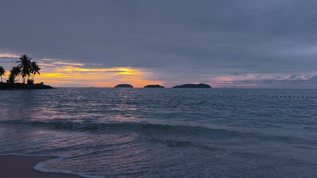 A breathtaking tropical beach scene at sunset . Silhouetted palm trees, remote isles, vibrant sky awash in pink, orange, and purple hues as the sun dips below the horizon in Tanjung Aru, Kota Kinabalu