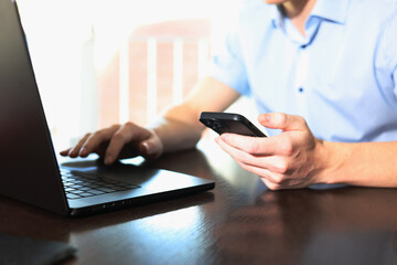 Male businessman working on laptop and holding smartphone in hand