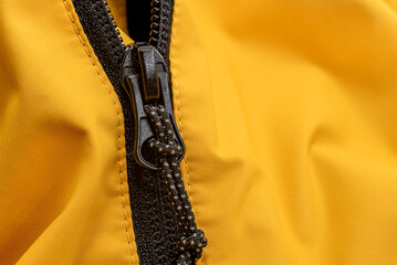 Dark lock with black zipper on yellow clothes close-up. Zipper