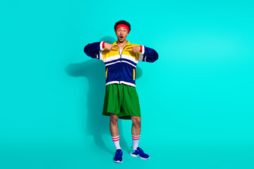 Young athletic man posing in vintage sportswear on vibrant turquoise background, showcasing retro style and active lifestyle.