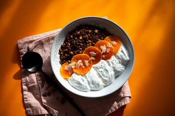 Granola with yogurt, fruits, chia seeds and nuts in a bowl. Chocolate granola with tangerine and yogurt, top view