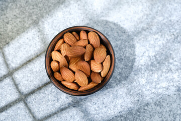 Bowl of whole almonds on light speckled stone background
